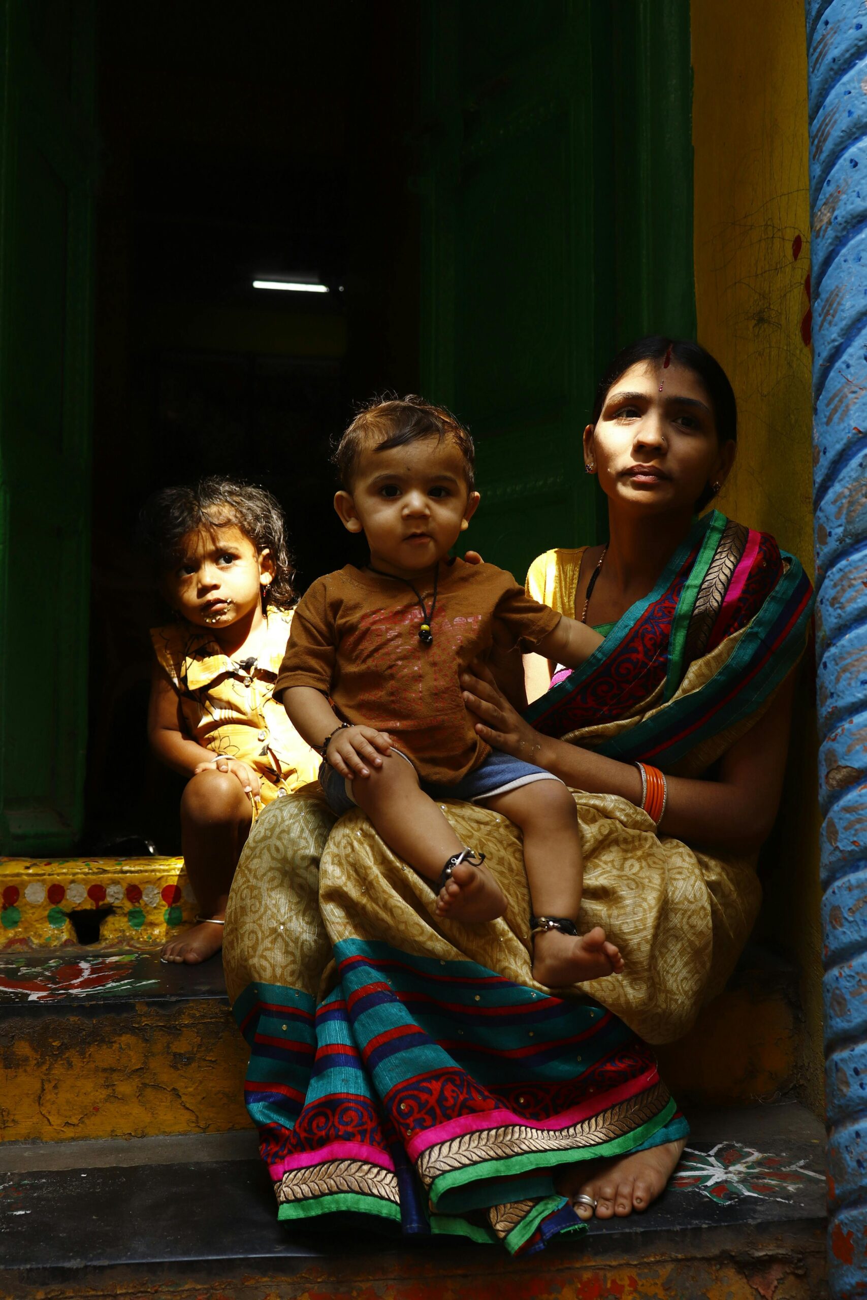 Home A mother with two children sitting on colorful steps in rural India.