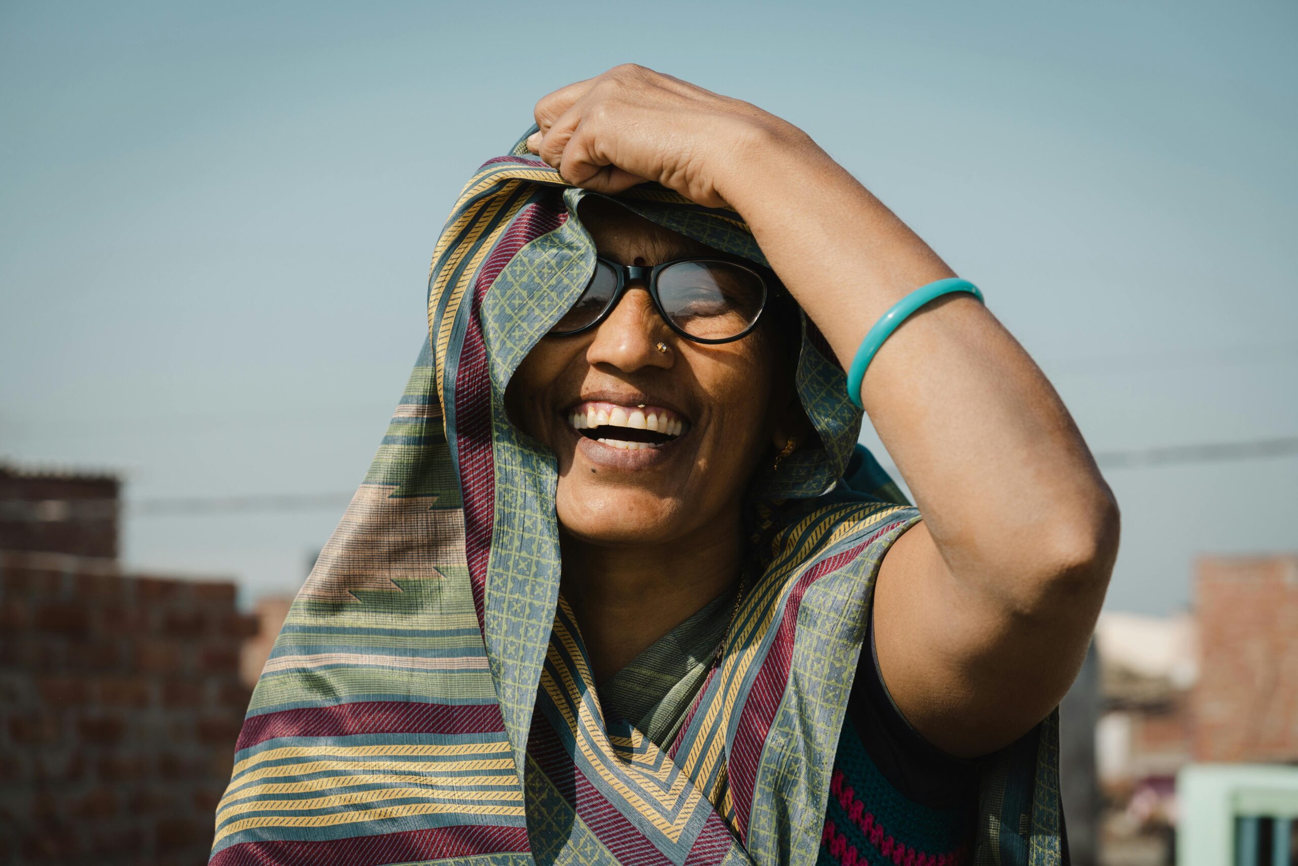 Home Joyful Indian woman smiling brightly under the sun, wearing traditional clothing.
